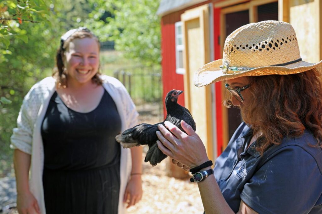 AWPP Coordinator Shea Steingass (right) holds a chicken as Brooke Davis looks on, at Brooke's farm.